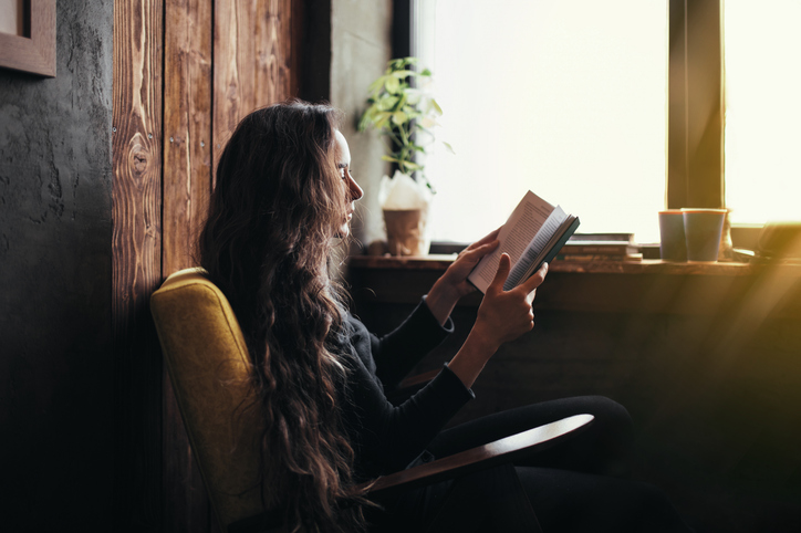 A woman sitting comfortably reading a book by a window, symbolizing the reflection and personal autonomy central to the ACA Code of Ethics and sound counseling practice.
